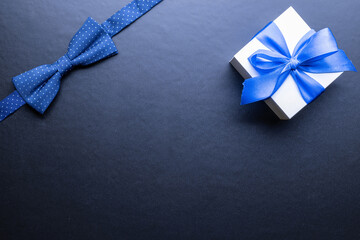 Father day present. White box with bow ribbon, blue bowtie or tie on dark background. Concept of Fathers Day greeting card, copy space for text.