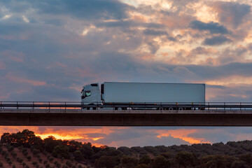 Refrigerated truck driving over a bridge with a dramatic sky in the background.