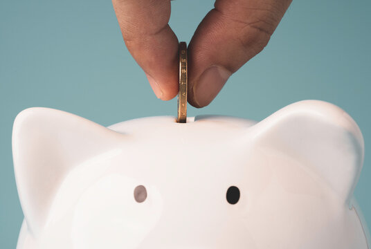 Hand putting coin to white piggy saving money, financial banking and bank deposit concept.