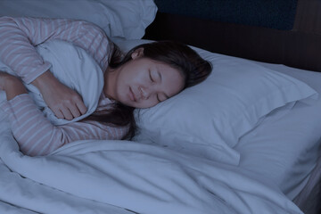 Obraz na płótnie Canvas An Asian Woman who has dark brown hair wearing long sleeve t-shirt is sleeping on the bed. in darkness room.
