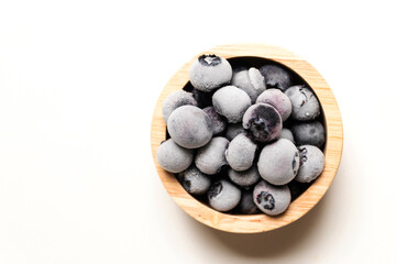 Frozen blueberries in wooden bowl isolated on white background.
