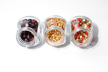 Three open glass jars of condiments. A mixture of five peppers, coriander and juniper berries. Isolate.