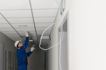 a worker installs a smoke and fire detector on the ceiling in the common hall of a residential building