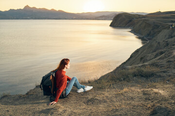 the traveler sits on the sand in the mountains and relaxes near the sea at sunset