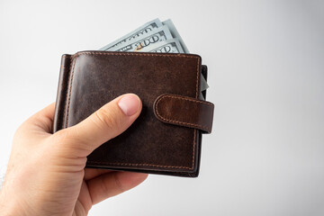 a man's hand holds a brown leather wallet with 100 dollars bills sticking out of it on a white background. The concept of money, wealth, wealth