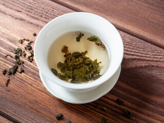 green tea is brewed in a white bowl on a wooden background. Dry tea leaves lie nearby. Top view