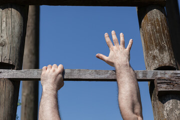 Strong male hands firm gripping  wooden ladder step, one hand reaching up, hanging, blue sky in...