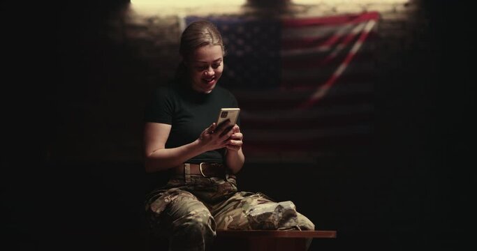 Delighted female soldier sitting on bench and making video call