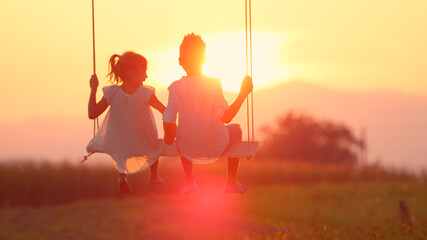 LENSE FLARE: Couple young children swaying and holding hands at golden sunset © helivideo