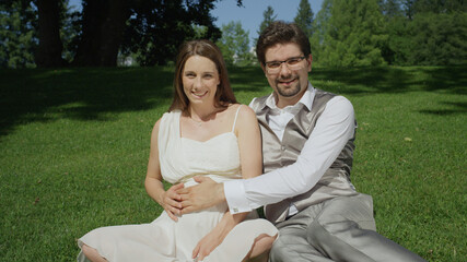 PORTRAIT: Smiling pregnant couple caressing her pregnant belly in sunlit park