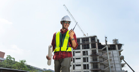 Asian man civil engineering wearing safety helmet and use radio for communication at construction site work.
