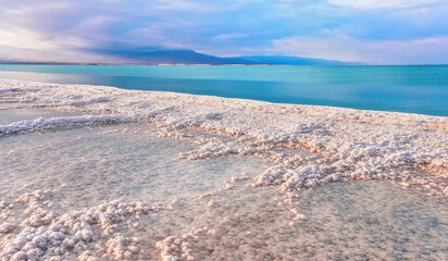 Morning sun shines on salt crystals formations, clear cyan green calm water near, typical landscape at Ein Bokek beach, Israel