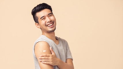 Portrait of Asian man showing his shoulder with bandage after getting a vaccination during covid-19...