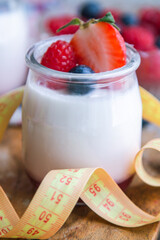 yogurt with raspberries and blueberries on wooden background with measuring tape, diet and food concept