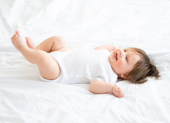 healthy 6 month baby boy smiling and lying on a white bedding at home.
