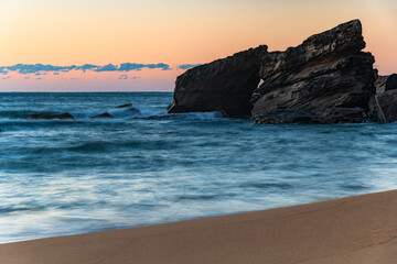 Sunrise at the seaside with soft orange pink sky and large rocky outcrop