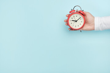 Red alarm clock in woman's hand on a blue background