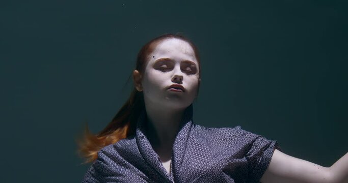Ethereal underwater portrait of young beautiful woman sleeping with eyes closed, then smiling at camera slow motion.