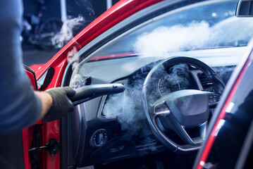 Car service worker cleans interiror with steam cleaner