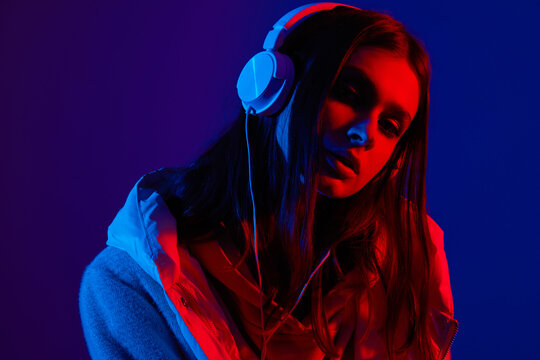 Young hipster woman with headphones listening to music in neon light.