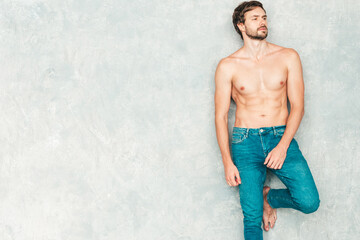Portrait of sporty handsome strong man. Healthy smiling athletic fitness model posing near gray wall in jeans. Confident sexy fashion male with naked nude torso. Lambersexual in studio