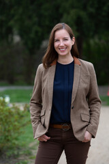 portrait of brunette woman in suit standing outside in park