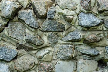 Cobblestone wall of large granite stones. A wall of stones fastened with cement mortar.