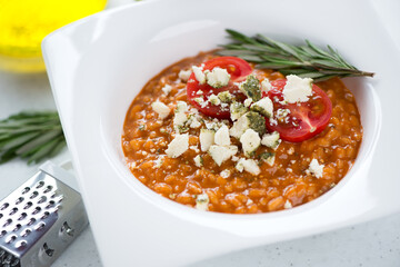Close-up of italian risotto with red pesto sauce and belper knolle cheese served in a white plate, selective focus