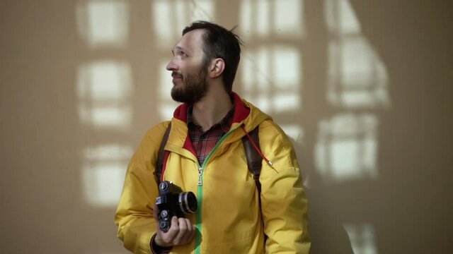 Adult male tourist photographer in yellow jacket taking photos with old film camera. Male backpacker with film camera traveling at the ancient city
