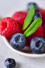 Raspberries, blueberries, mint leaves on a saucer, on a gray background, close-up.