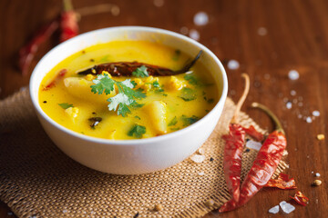 Close-up of healthy curry of yogurt (curd) and potato (Dahi Aloo or Aaloo ) an Indian Classical dish,  served in a white ceramic bowl. Over Wooden Background with red chilies and salt. Top view.