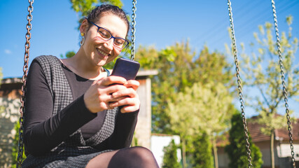 woman sitting on a swing and smiling while using phone