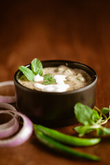 Close-up of Methi-Matar-Malai with white curry with fresh green chilies, mint leaves, and onions. A popular, delicious Indian recipe in a black bowl over wooden background.