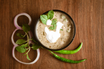 Close-up of Methi-Matar-Malai with white curry with fresh green chilies, mint leaves, and onions. A popular, delicious Indian recipe in a black bowl over wooden background.