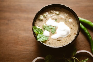 Close-up of Methi-Matar-Malai with white curry with fresh green chilies, mint leaves, and onions. A popular, delicious Indian recipe in a black bowl over wooden background.