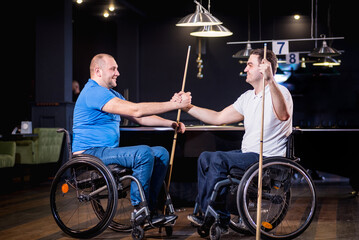 Adult men with disabilities in a wheelchair play billiards in the club
