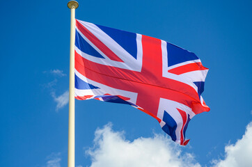 Flags of Great Britain waving on flagpole. United Kingdom UK flag flying on a pole. Brexit. Union jack flag against blue sky.