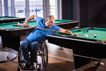 Adult man with disability in a wheelchair play billiards in the club