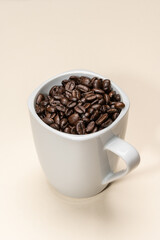 Roasted coffee beans inside a white cup on a beige background.