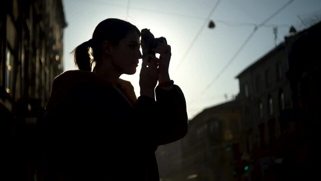 Silhouette of young woman photographer, taking photos on the street with beautiful sunset