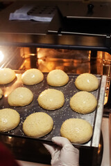 Baker puts their buns in the oven, which he had previously greased with butter and sprinkled with sesame seeds. Homemade baked goods and confectionery production. Home cooking concept. Vertical photo