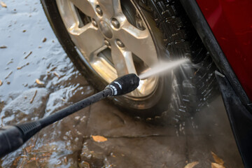 Washing a red car tires with high pressure washer cleaner.