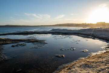 Naklejka premium reflection in a puddle of the sun setting on the rocks at the beach 
