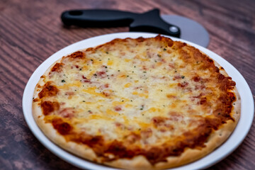 Close up and selective focus of a home cooked thin crust four cheese pizza on a white plate on a wooden table