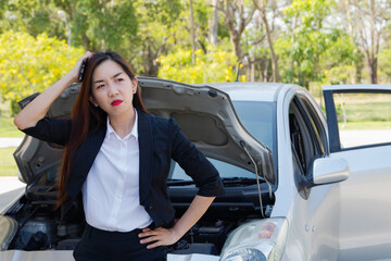 Businesswoman standing in front of her saloon, opened the hood, made her face tense, scratching her head, frustrated, because of the problem of getting lost and damaged cars at the same time.