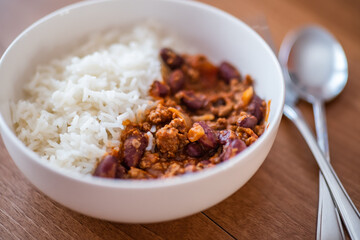 Close up and selective focus of meat chilli concarne and white rice in a white bowl on a wooden surface with intentional shallow depth of field and bokeh