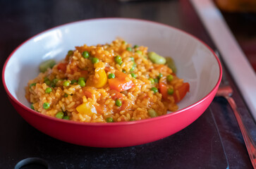 Close up of a healthy, nutritious and homemade vegetable paella in a red dinner bowl with selective focus, shallow depth of field and bokeh