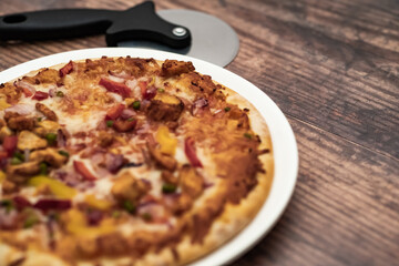 Close up and selective focus of a home cooked thin crust sweet chilli chicken pizza on a white plate on a wooden table