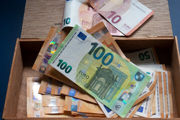 Durcheinander von verschiedene Euro Banknoten,fünfzig Euro Schein und 100 Euro Schein,in einer alten Zigarrenkiste vor blauen Hintergrund