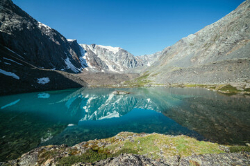 Snowy mountain reflected in clear water of glacial lake. Beautiful sunny landscape with glacier reflection in water surface of mountain lake under clear sky. Snow on rock reflected in mountain lake.